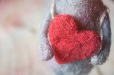 Büyük kırmızı bir kalbin ellerindeki yünden yapılmış oyuncak fare.