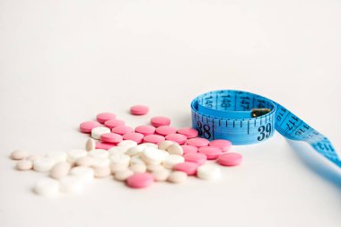 blister with tablets and tied with measuring tape, the concept of taking drugs for weight loss and maintain the figure, the harm of supplements for weight loss, isolated on white background