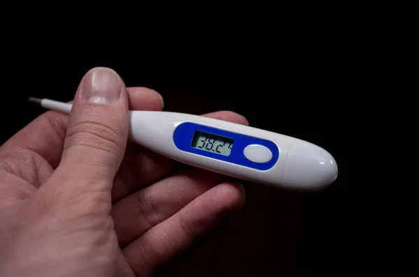 electronic thermometer in hand shows high temperature on the dark background, fever, disease