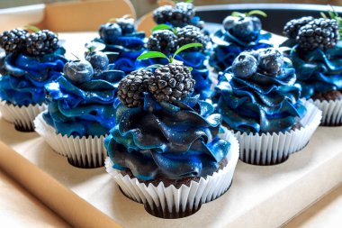 Mavi kremalı, yaban mersinli, böğürtlenli, el yapımı pastalı, yakın plan keklerden oluşan bir set.