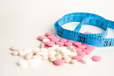blister with tablets and tied with measuring tape, the concept of taking drugs for weight loss and maintain the figure, the harm of supplements for weight loss, isolated on white background