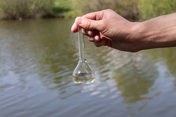 hand holding test tube for analyses with water on the background of the reservoir, the concept of water purity, pollution of water bodies, checking the quality of drinking water in cities, environmental