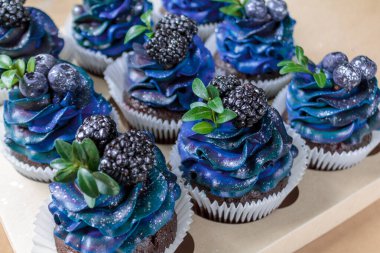 Mavi kremalı, yaban mersinli, böğürtlenli, el yapımı pastalı, yakın plan keklerden oluşan bir set.