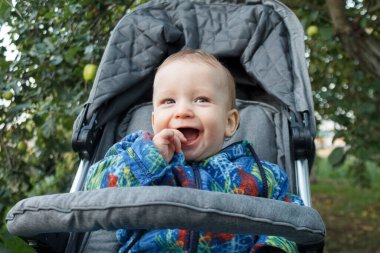 Bir yaşına kadar neşeli küçük bir bebek bebek bebek arabasında oturuyor ve mutlu bir şekilde gülümsüyor. Yazın güzel havalarda ailesiyle sokakta gülüyor ve oynuyor.