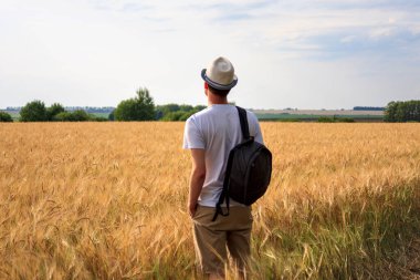 Sırt çantalı genç gezgin gün batımında sahada duruyor ve başka yere bakıyor. Seçim özgürlüğü, gelecek, seyahat ve macera kavramı.