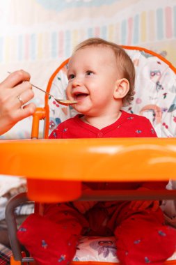 Neşeli küçük bir bebek, bir yaşına kadar yüksek bir sandalyede oturur ve beslenmek için ebeveynler kaşıkla beslenir, ilk yem, bebek maması seçimi...