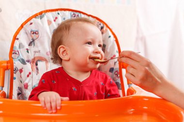 Küçük bir çocuk kaşıkla yer ve çocuk odasındaki beslenme masasının kenarına oturur, kirlidir ve besin, bebek maması konsepti, tamamlayıcı gıdalar, ilk kaşık