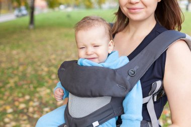 Küçük bebek askılı ergorace bir annede oturuyor, çocuğu sırtında yük olmadan dik bir pozisyonda taşıyor.