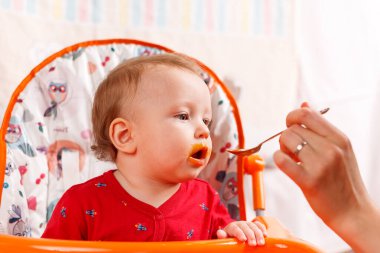 Küçük bir çocuk kaşıkla yer ve çocuk odasındaki beslenme masasının kenarına oturur, kirlidir ve besin, bebek maması konsepti, tamamlayıcı gıdalar, ilk kaşık