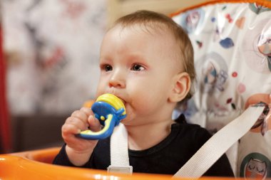 Küçük bir çocuk kaşıkla yer ve çocuk odasındaki beslenme masasının kenarına oturur, kirlidir ve besin, bebek maması konsepti, tamamlayıcı gıdalar, ilk kaşık, dişleyici, meyve emziği ile lekelenir.