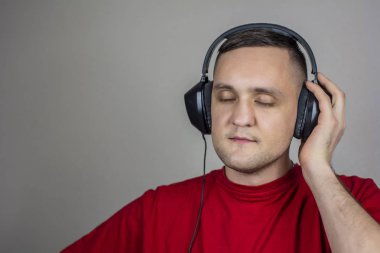 Kırmızı tişörtlü genç adam kulaklıkla müzik dinliyor.