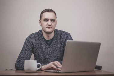  Dizüstü bilgisayarda çalışan genç bir adam ve arka planda bir fincan kahve. 