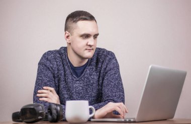  Dizüstü bilgisayarda çalışan genç bir adam ve arka planda bir fincan kahve. 