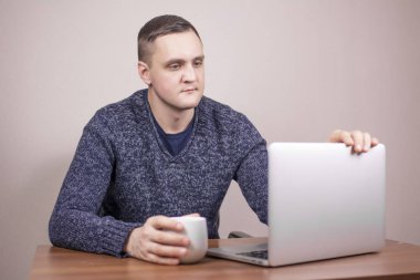  Dizüstü bilgisayarda çalışan genç bir adam ve arka planda bir fincan kahve. 