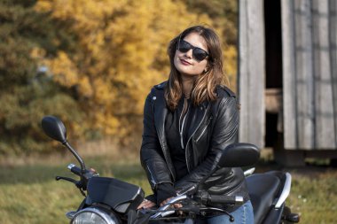 Deri ceketli, gözlüklü motosikletli genç bir kız.