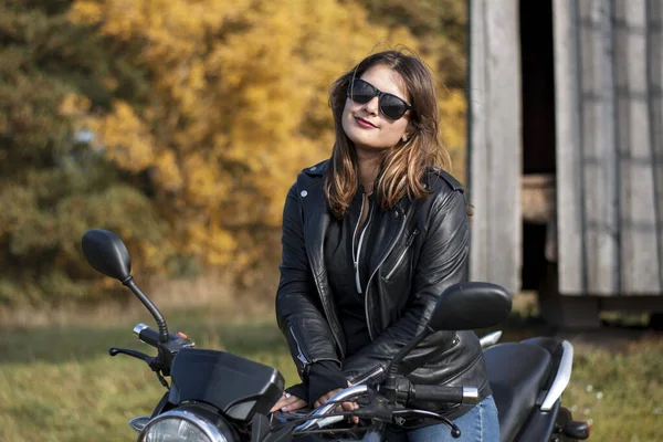 Deri ceketli, gözlüklü motosikletli genç bir kız.