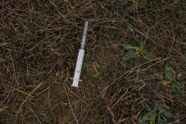 Küçük bir tıbbi beyaz şırınga yeşil, uzun çimenlerin üzerinde yatıyor. 