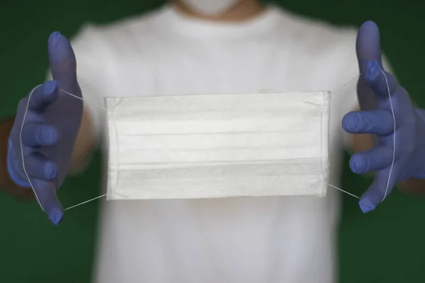 guy in medical gloves holding a white medical mask on a green background