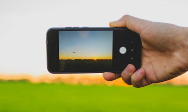 modern telefon kırmızı günbatımının ve tarlanın fotoğraflarını çekiyor.