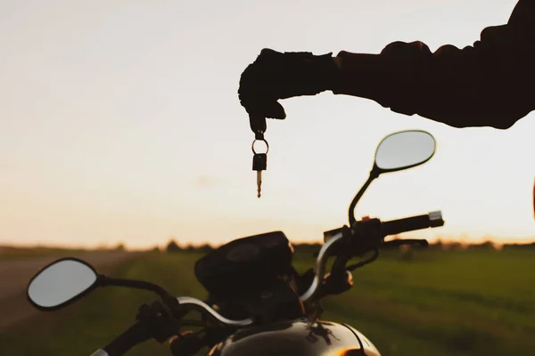 Motosikletlerin arka planında siyah bir ulaşım anahtarı tutan adam.