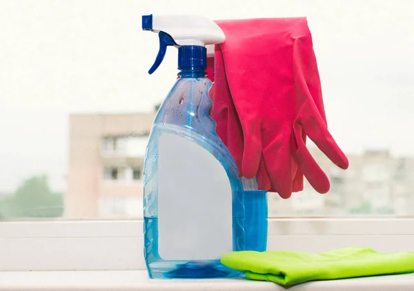 blue container with sprayer for washing windows and pink rubber glove on a blurred background