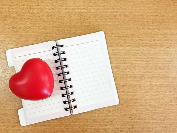 Rött hjärta plast på öppna anteckningsbok och trä bord — Stockfoto