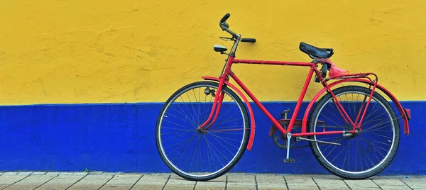 Bicicleta vermelha na frente da parede amarela e azul — Fotografia de Stock