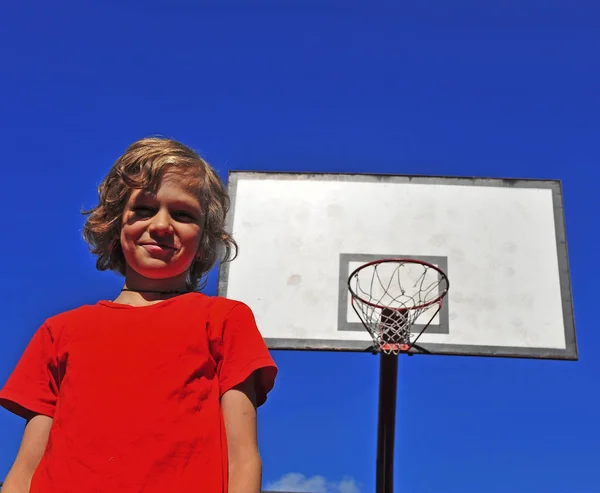 पृष्ठभूमि पर बास्केटबॉल हूप के साथ खुश मुस्कुराते हुए लड़का — स्टॉक फ़ोटो, इमेज
