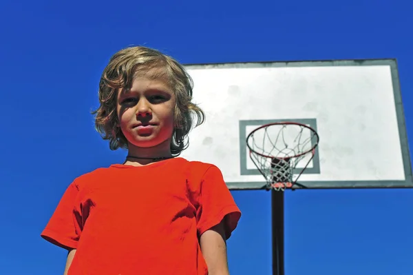 Niño en camiseta roja con aro de baloncesto en el fondo — Foto de Stock