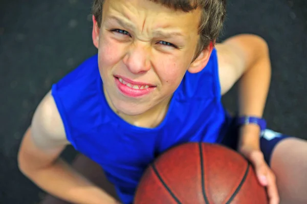 Sonriente niño con una pelota de baloncesto sentado en la cancha —  Fotos de Stock