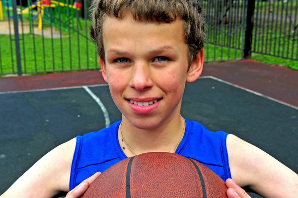 Usměvavý chlapec s basketbal sedí na kurtu — Stock fotografie