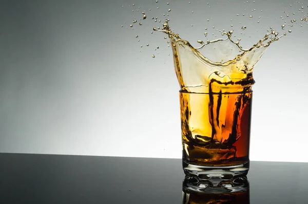 Splash konyak gri arka plan üzerinde şeffaf cam. Turuncu buzlu içecek.