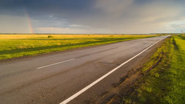 Islak asfalt yol yağmur bulutları gökkuşağı ile arka plan üzerinde işaretleme ile sonra. Bahar ya da yaz manzara seyahat Tema.