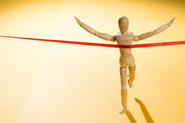 Adam bitiş çizgisinde. Ahşap bebek ve kırmızı kurdele.