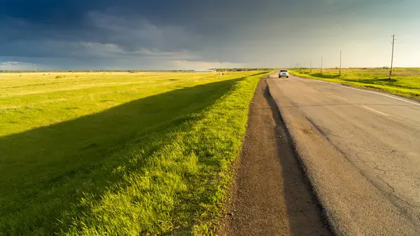Yağmur sonra gökyüzüne karşı alanın ortasında bir ülke yolda arabadır.