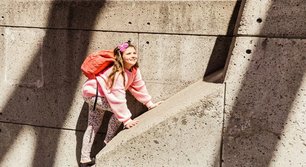 Bonita vista de la sonrisa feliz y alegre niña caminando en la pared de hormigón en el soleado día de primavera —  Fotos de Stock