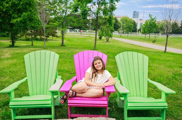 Feliz sorriso menina sentada na cadeira confortável rosa e desfrutando de seu tempo de lazer no parque ao ar livre — Fotografia de Stock