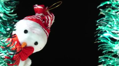 Kırmızı şapkalı ve fiyonklu sevimli kardan adam olay yerinden sana bakıyor. Siyah arka planda Noel tebriği. Şenlik havası. Yeni yıl ya da tatil teması