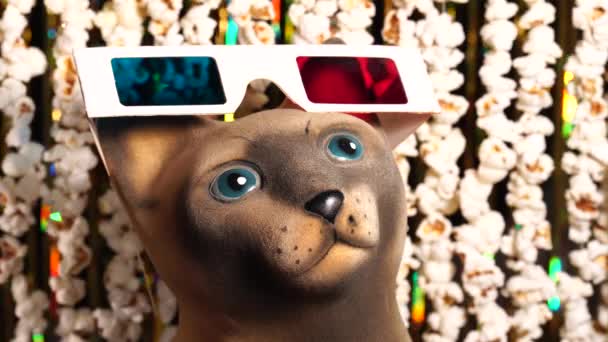 Üç boyutlu gözlüklü kedi heykelciği. Patlamış mısır ve altın parıltılı süslemelerden oluşan çelenklerin dinamik arkaplanı. Film haberleri için patlamış mısır çelenkleri. Film izlemek için davetiye. 4K video — Stok video