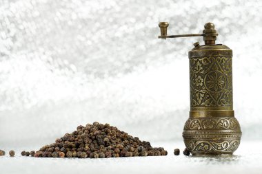 Gümüş arka planda kara biber ve antika bir değirmen. Baharat öğütücü ve bir yığın biber. Paketleme için örnek. Yakın plan fotoğraf.