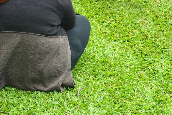 Backside of a fat girl who sitting on green grass yard floor ground.