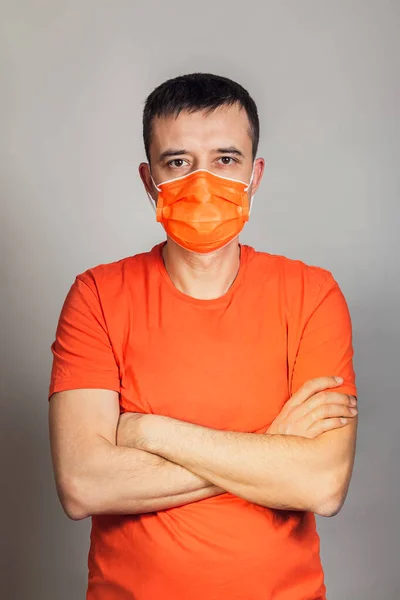 Un bărbat european, într-un tricou portocaliu, cu o mască medicală portocalie pe față, și-a încrucișat brațele peste piept. Anxietatea și teama de răspândirea virusului . — Fotografie, imagine de stoc