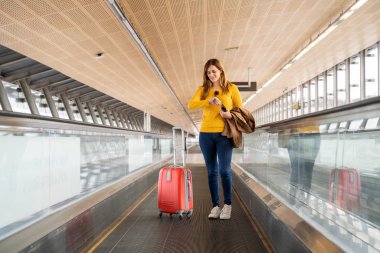 Beautiful young woman looking at her watch at the airport or station with her luggage. Travel and holiday concept.