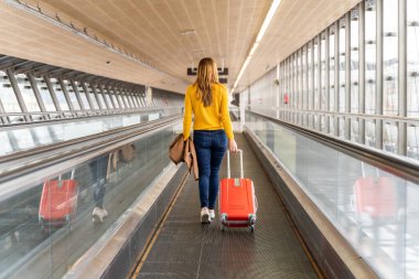 Beautiful young woman walking backwards to the airport or station with her luggage. Travel and holiday concept.