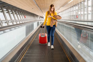 Beautiful young woman looking at her watch at the airport or station with her luggage. Travel and holiday concept.