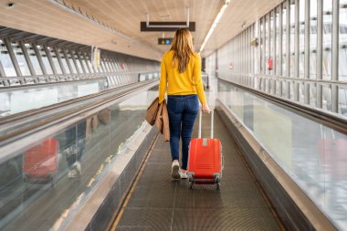 Beautiful young woman walking backwards to the airport or station with her luggage. Travel and holiday concept.