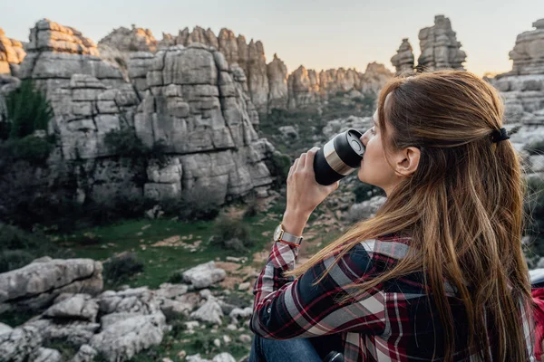 Young woman explorer drinking coffee from a thermos flask with the mountains in the background. Concept of adventure, excursion and trips.