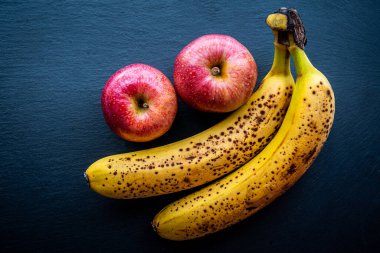 Sağlıklı ve doğal besin kavramının karanlık arka planında bazı muz ve elmaların üst görüntüsü.