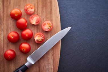 Üstünde bıçak olan kiraz domateslerinin üst görüntüsü. Koyu renkli bir masanın üzerindeki ahşap olan. Vejetaryen ve sağlıklı gıda kavramı.