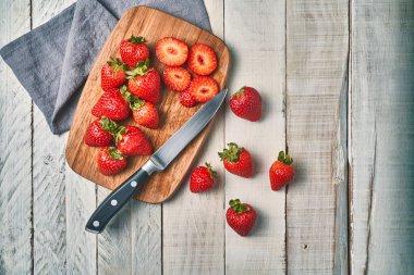 Beyaz bir masada tahta bir tahtanın üzerinde taze kesilmiş kırmızı çileklerin üst görüntüsü..